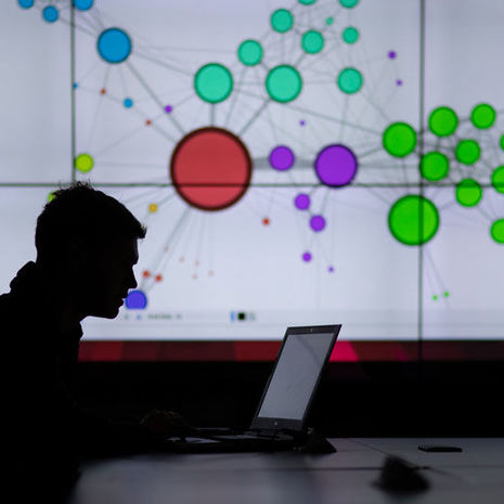 man on a laptop in silhouette with data visualization on screen